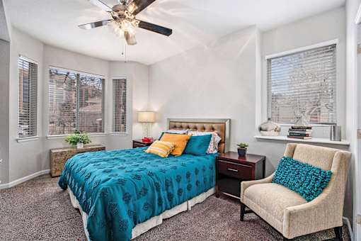A bedroom with a bed, chair, and ceiling fan.