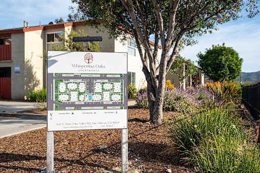 A sign for Whispering Oaks Apartments stands in front of a building.
