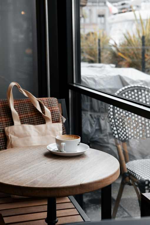 A cup of coffee sits on a saucer on a wooden table.