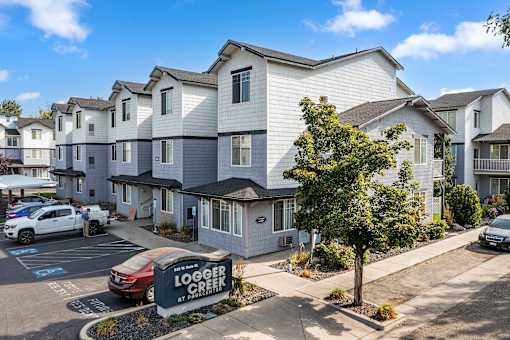 A sunny day at the Logger Creek Apartments with cars parked in the lot.