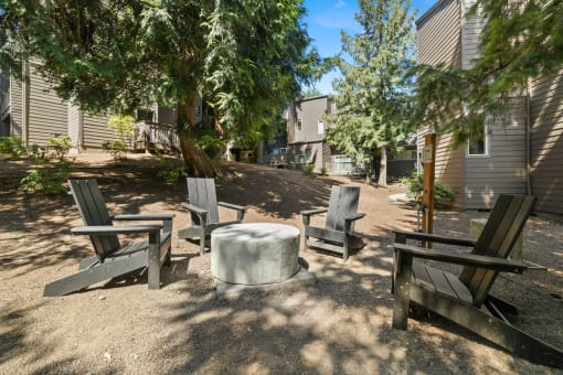Firepit with four chairs and a table in the middle of a dirt area with trees  at Larkspur West Linn, Oregon