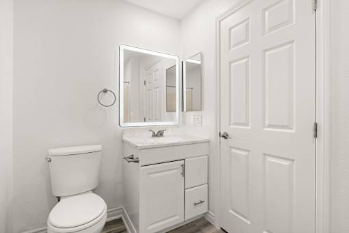 A white bathroom with a toilet, sink and mirror.