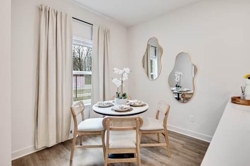A dining room with a table set for two and a vase of white flowers.