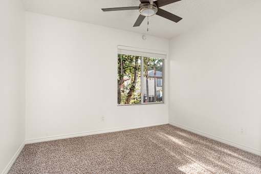 A room with a ceiling fan and a window showing trees and a building outside.