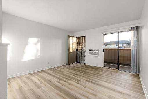 A room with wooden floors and a white wall with a door leading to a balcony.