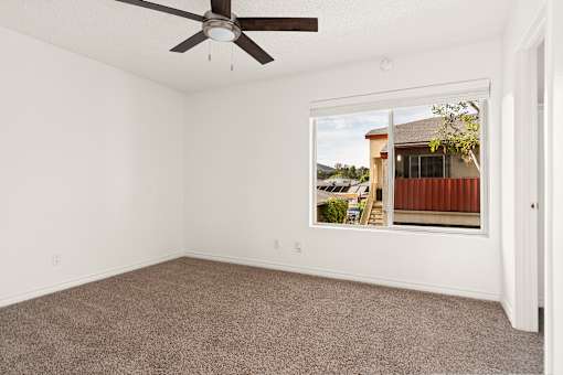 Empty room with a ceiling fan and a window showing a view of a house.