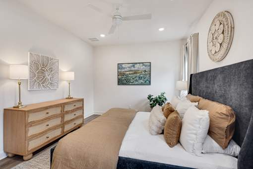 A bedroom with a large bed, a wooden dresser, and a painting on the wall.