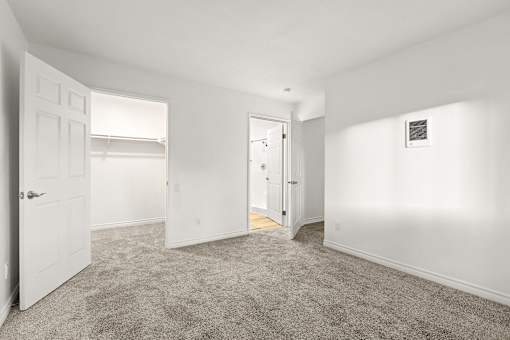 A room with white walls and carpeted floor with two doors.