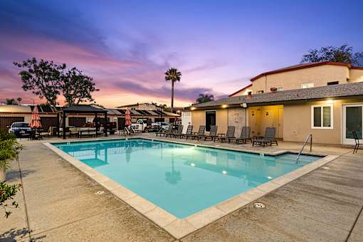A pool surrounded by chairs and a building in the background.