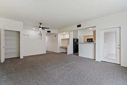 A spacious room with a ceiling fan and a kitchenette in the background.
