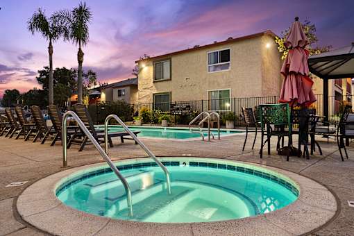 A hot tub sits in the middle of a pool surrounded by chairs and umbrellas.
