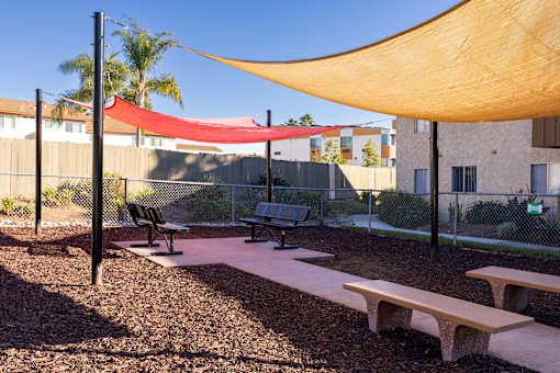 A playground with a red and yellow shade structure.