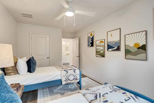 A bedroom with a bed, pillows, a ceiling fan, and pictures on the wall