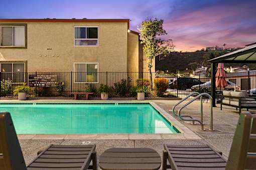 A pool surrounded by lounge chairs and a building in the background.