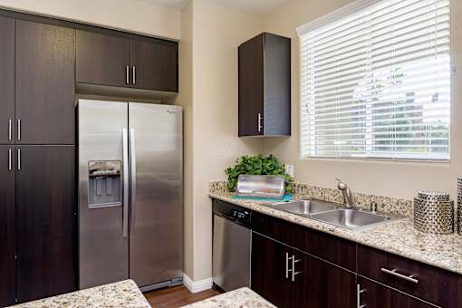 A kitchen with a stainless steel refrigerator and dark brown cabinets.