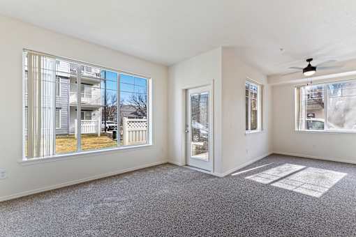 A spacious room with a grey carpet and a ceiling fan.