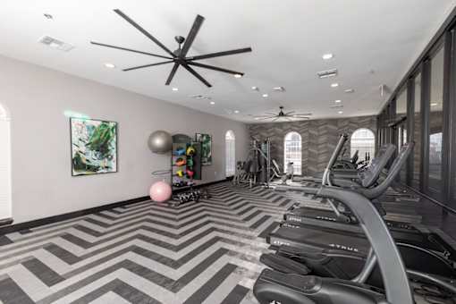 A gym with treadmills, elliptical machines, and a ceiling fan.
