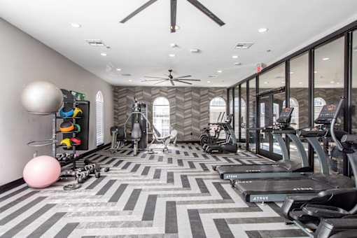 A gym with treadmills, exercise bikes, and a fan.
