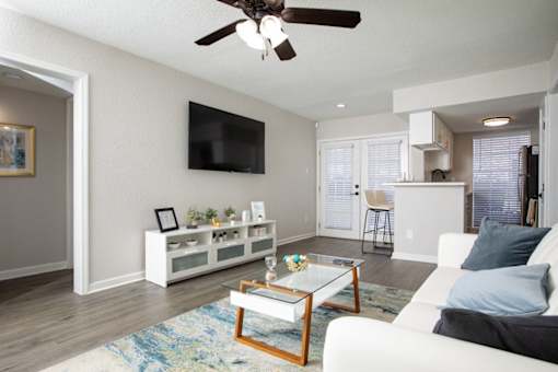 A living room with a white couch, a glass coffee table, and a flat screen TV mounted on the wall.