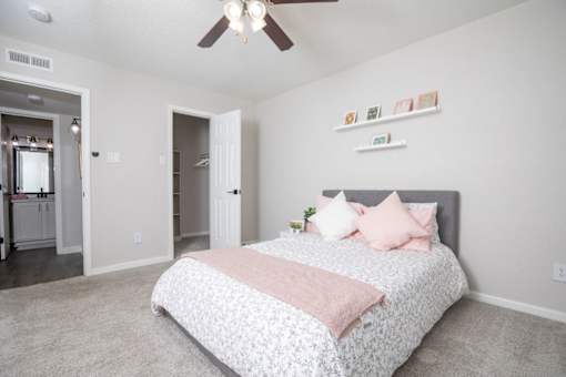 A bedroom with a bed, pink pillows, and a ceiling fan.