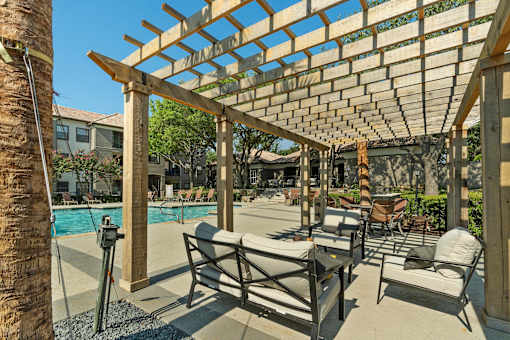 A wooden pergola over a poolside lounge area.