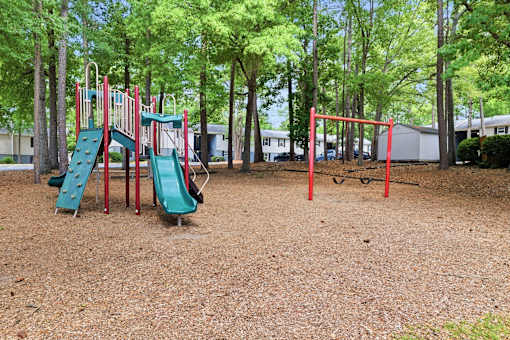 A playground with a red swing set and a green slide.