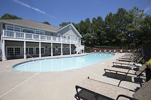 A large swimming pool is surrounded by sun loungers and a building with a balcony.