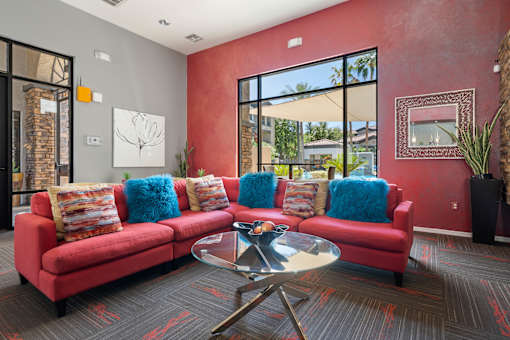 A red couch with blue pillows sits in a room with a glass table in front of it.