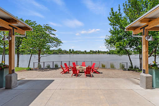 A patio with red chairs and a view of a lake.