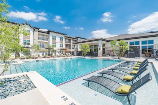 a swimming pool with lounge chairs in front of an apartment building