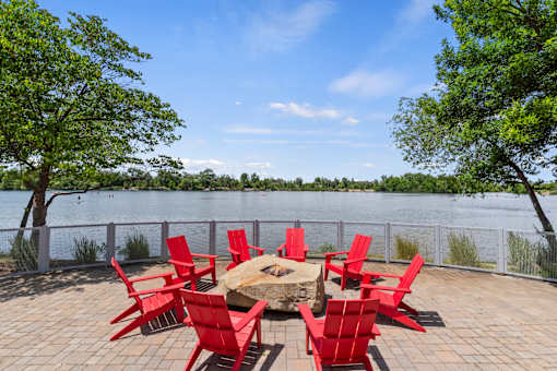 A table surrounded by red chairs is on a patio overlooking a body of water.
