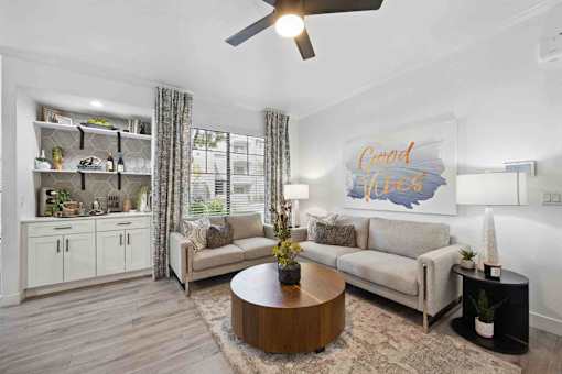 A living room with a grey couch, a wooden coffee table, and a painting that says