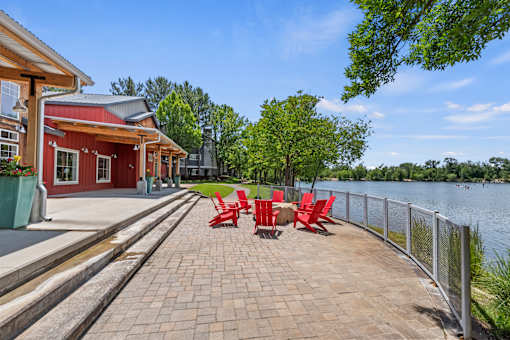 A red building with a white roof is situated next to a body of water with a red bench in front of it.