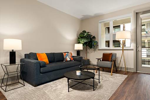 A living room with a grey couch, a black coffee table, and a large window.
