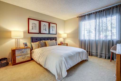 A bedroom with a large bed, two lamps, and two pictures on the wall.