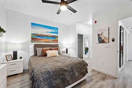 A bedroom with a bed, a ceiling fan, and a painting on the wall.