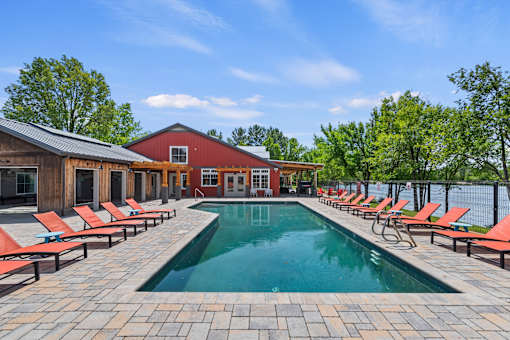 A pool surrounded by red lounge chairs and a wooden building.