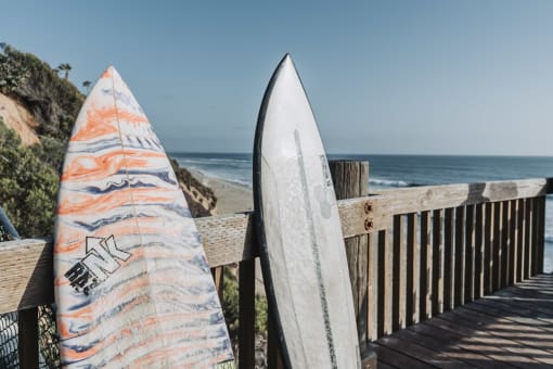 two surfboards leaning against a fence next to the beach