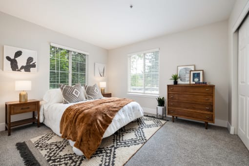Spacious bedroom with white bedding and patterned throw at Canyon Creek Apartments, Wilsonville, OR