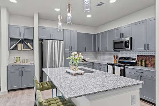A kitchen with a granite countertop and grey cabinets.