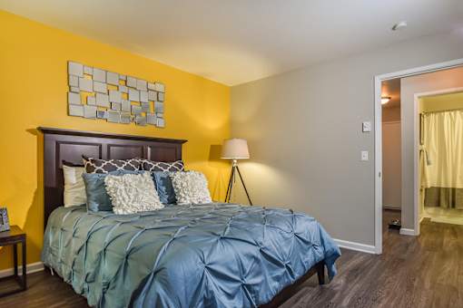 A bedroom with a bed, lamp, and artwork on the wall.