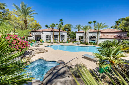 A pool surrounded by palm trees and apartments in the background.