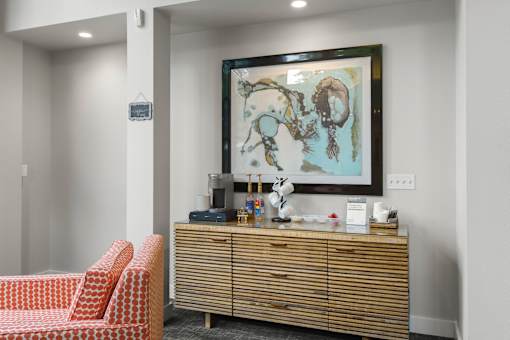A painting hangs on the wall above a wooden cabinet with a red couch in front of it.