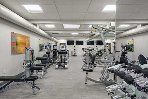 A gym with a variety of equipment including treadmills, weights, and exercise machines.