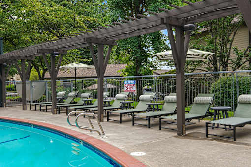 A pool with a wooden pergola and lounge chairs.