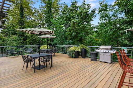 A wooden deck with a table and chairs and a grill.