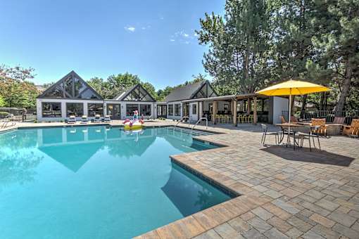 A large outdoor swimming pool with a yellow umbrella and a house in the background.