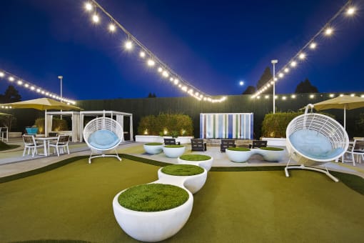 a lounge area with chairs and tables under lights at night