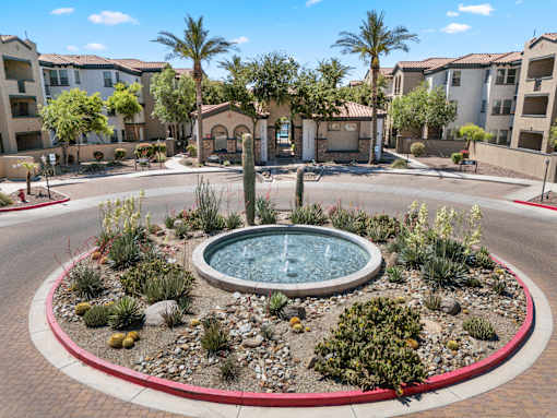 A fountain in the middle of a landscaped area with apartment buildings in the background.