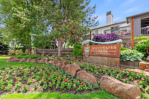 A sign for Whitewater Park Apartments stands in front of a flower bed.